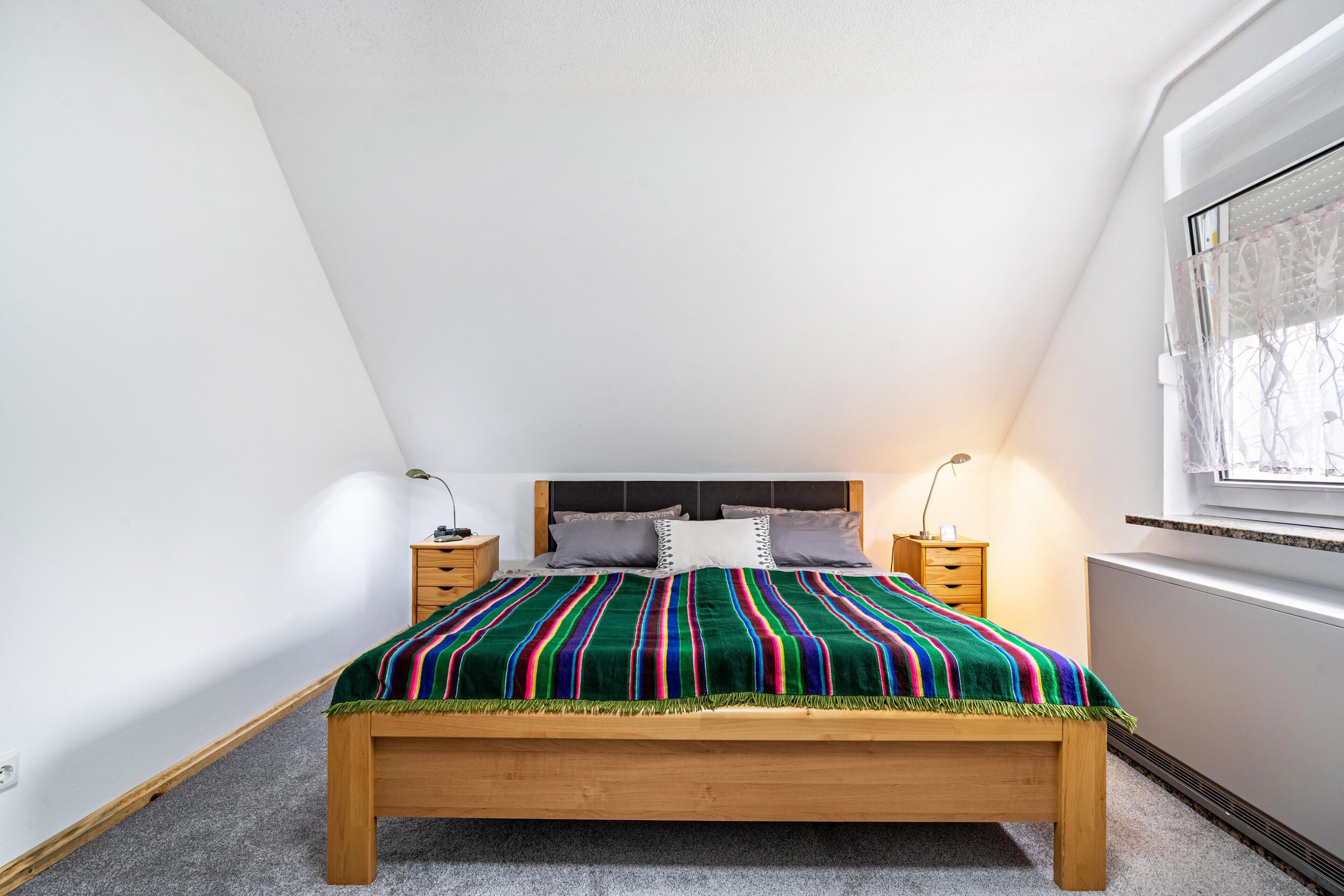 A bedroom with a wooden bed, a colorful striped blanket, two bedside tables, and a window with a view.