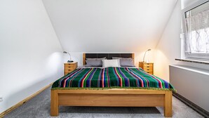 Ein Schlafzimmer mit einem hölzernen Bett, einer farbenfrohen, gestreiften Decke, zwei Nachttischen und einem Fenster mit Blick.