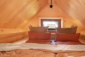 Une chambre confortable située dans les combles, avec des murs en bois, un plafond en pente et une fenêtre au fond.