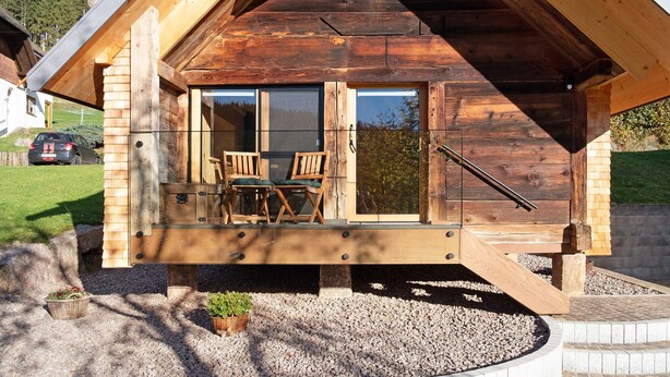 Eine Holzhütte mit einem Balkon, einem Tisch mit Stühlen und einem kleinen Garten.
