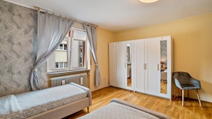 Une chambre avec deux lits, une armoire, une chaise et une fenêtre avec des rideaux.