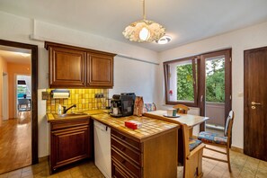 A kitchen with wooden cabinets, a coffee maker, and a window with a view of greenery.
