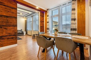 A dining area with a wooden table, grey chairs, and large windows with curtains.