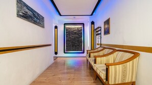 Un pasillo con suelo de madera, una puerta con pared texturizada y un rincón de estar con sillones tapizados.