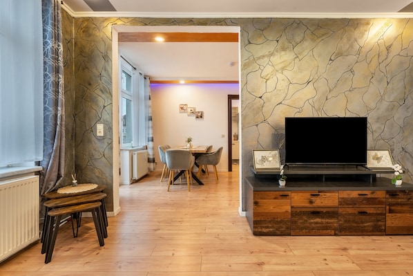 A modern living room with a flat-screen TV, wooden furniture, and a stone-patterned wall.