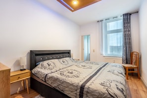 A bedroom with a bed, bedside table, chair, window with curtains, and a ceiling light.