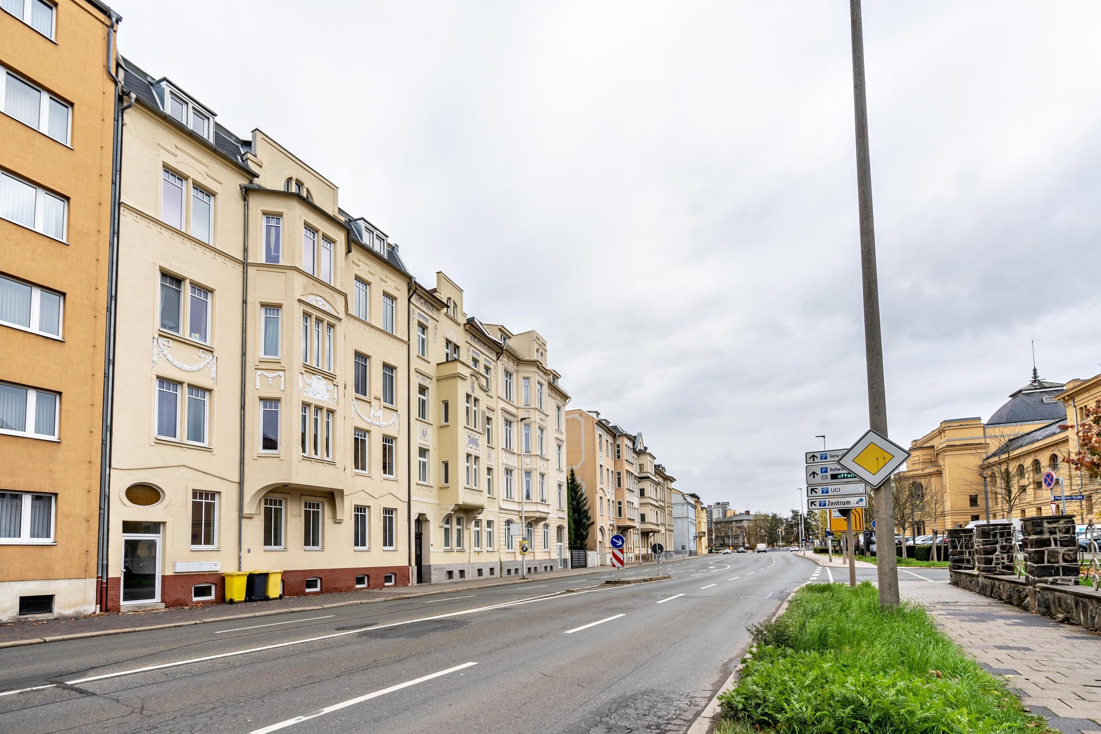 Calle con edificios de varios pisos, una vía despejada y señales de dirección.