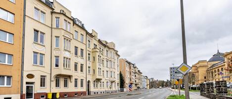 Calle con edificios de varios pisos, una vía despejada y señales de dirección.