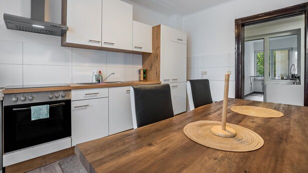 A modern kitchen with white cabinets, a wooden countertop, a built-in oven, and a dining table with two woven placemats. - Apartment 'Ferienwohnung Am Theaterplatz' with Wi-Fi (Gera)