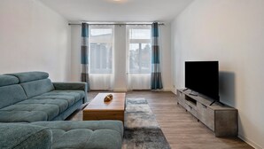 A living room with a sofa, a coffee table, a TV on a stand, and a window with curtains. - Apartment 'Ferienwohnung Am Theaterplatz' with Wi-Fi (Gera)