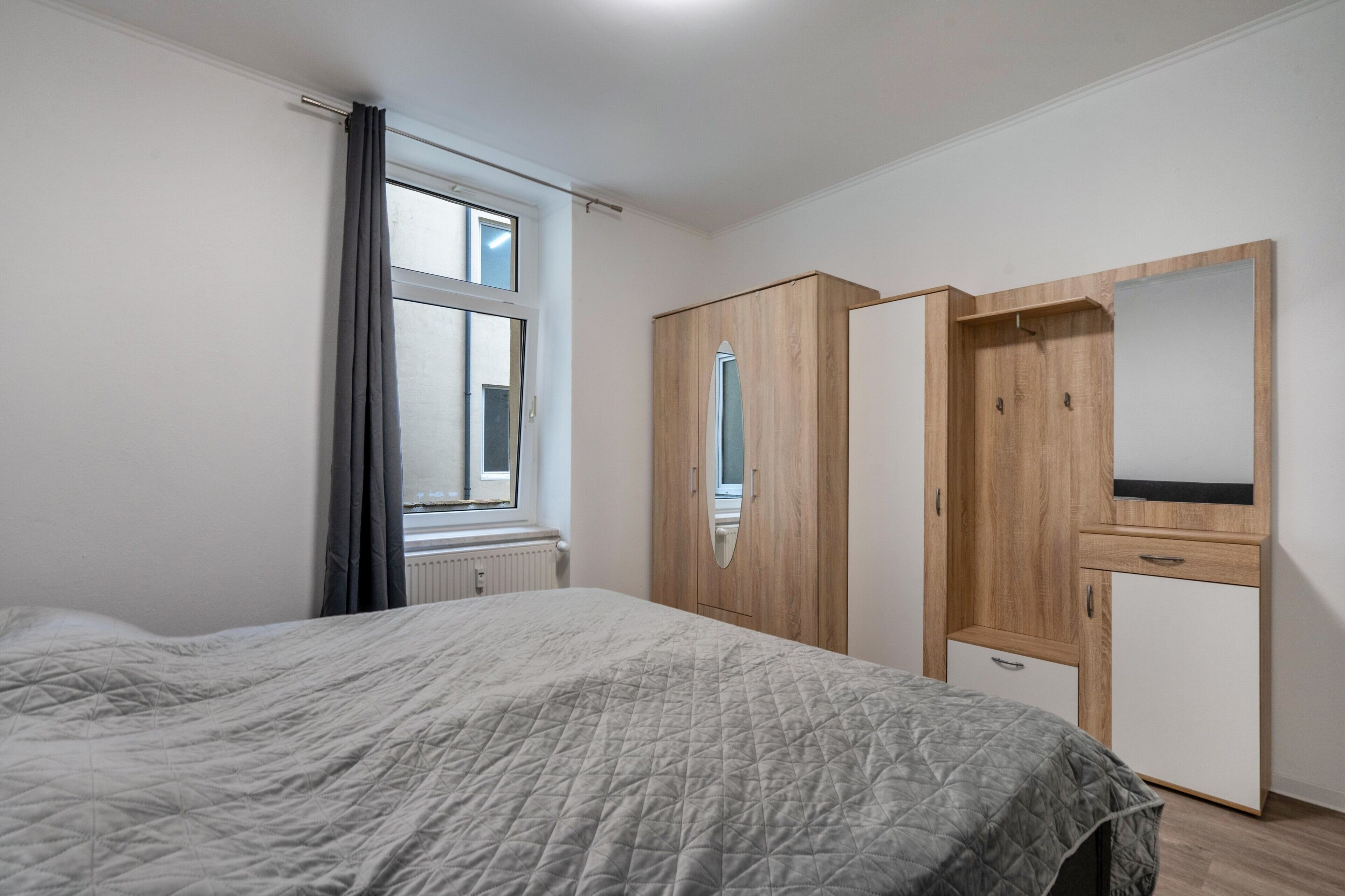 A bedroom with a bed, a wardrobe, a mirror, and a window.
