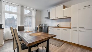A modern kitchen with white cabinets, a wooden dining table, and a view through large windows. - Apartment 'Ferienwohnung Am Theaterplatz' with Wi-Fi (Gera)