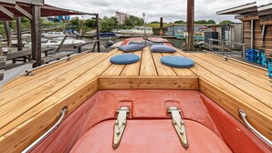 Een schepdek met een houten vloer, twee blauwe kussens en metalen reling.