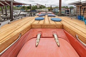 Un pont de bateau avec un plancher en bois, deux coussins bleus et des garde-corps en métal.
