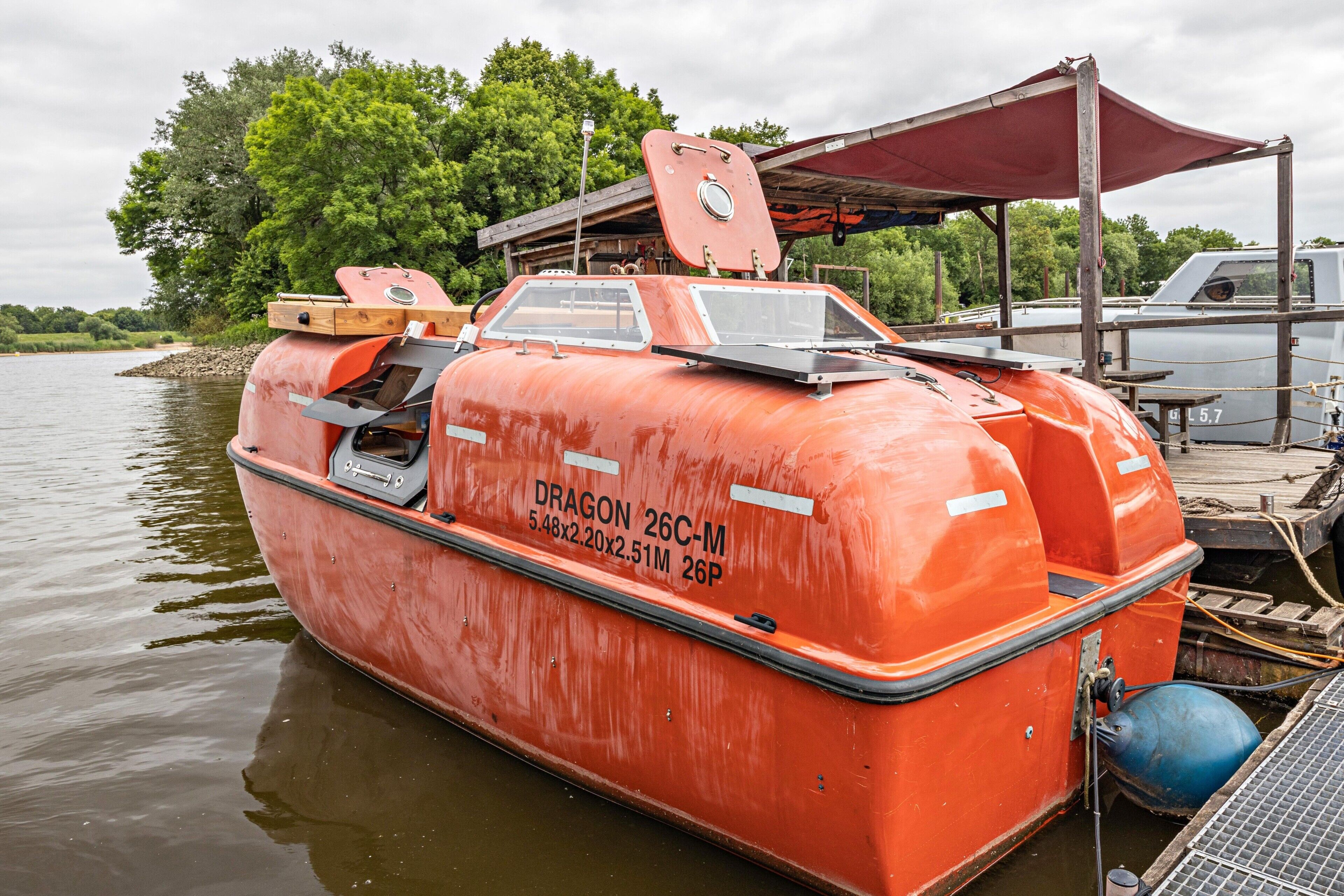 En stillastående, orangefärgad båt med texten ”DRAGON 26C-M” och måtten ”5,48x2,20x2,51 m, 26P” på sidan.