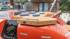 Een boot met een houten dek, een klein afgesloten gedeelte met kussens, en een reddingsboei.