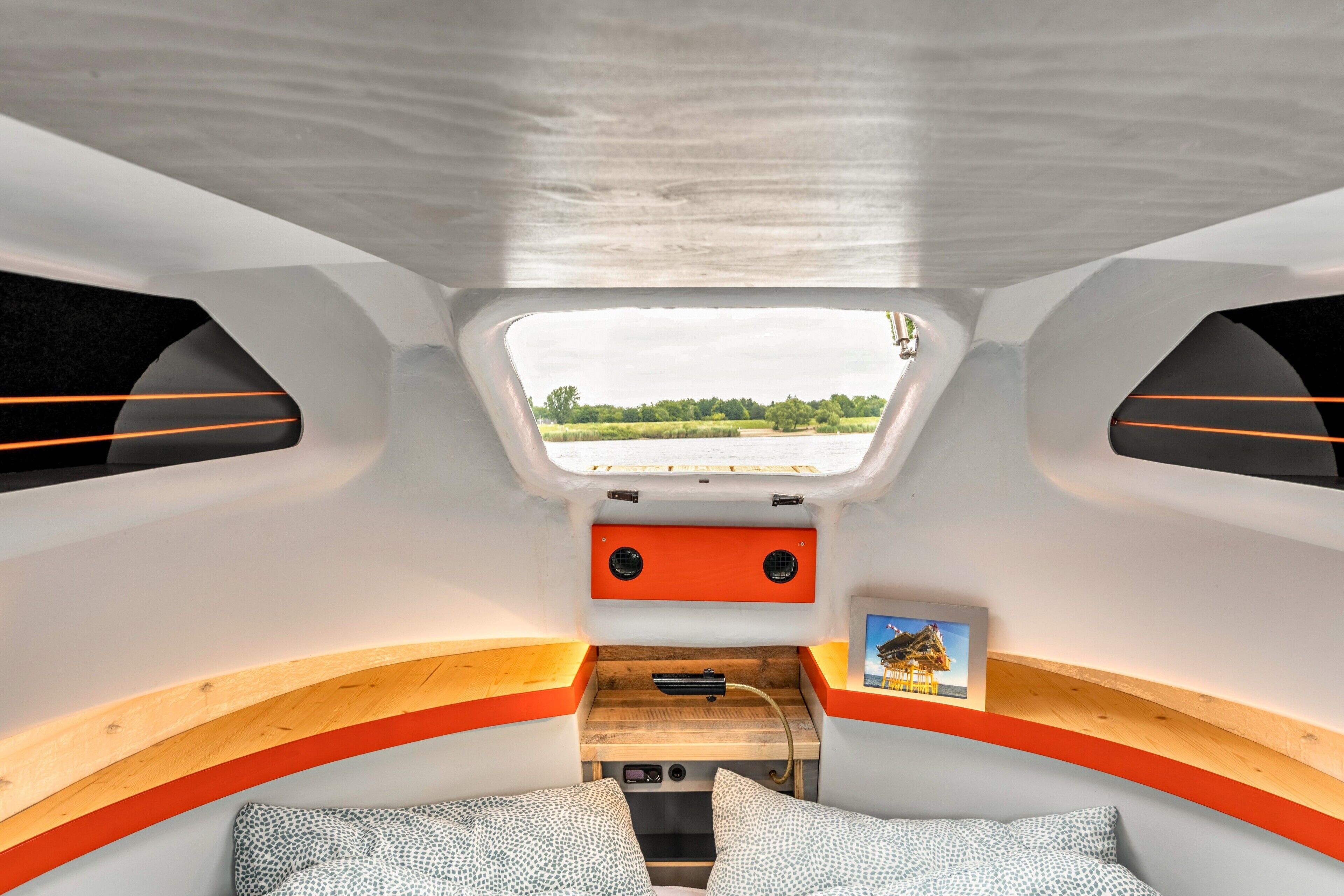 A compact interior with a small bed, seating area, and a window providing a view of the outdoors.