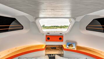 A compact interior with a small bed, seating area, and a window providing a view of the outdoors.