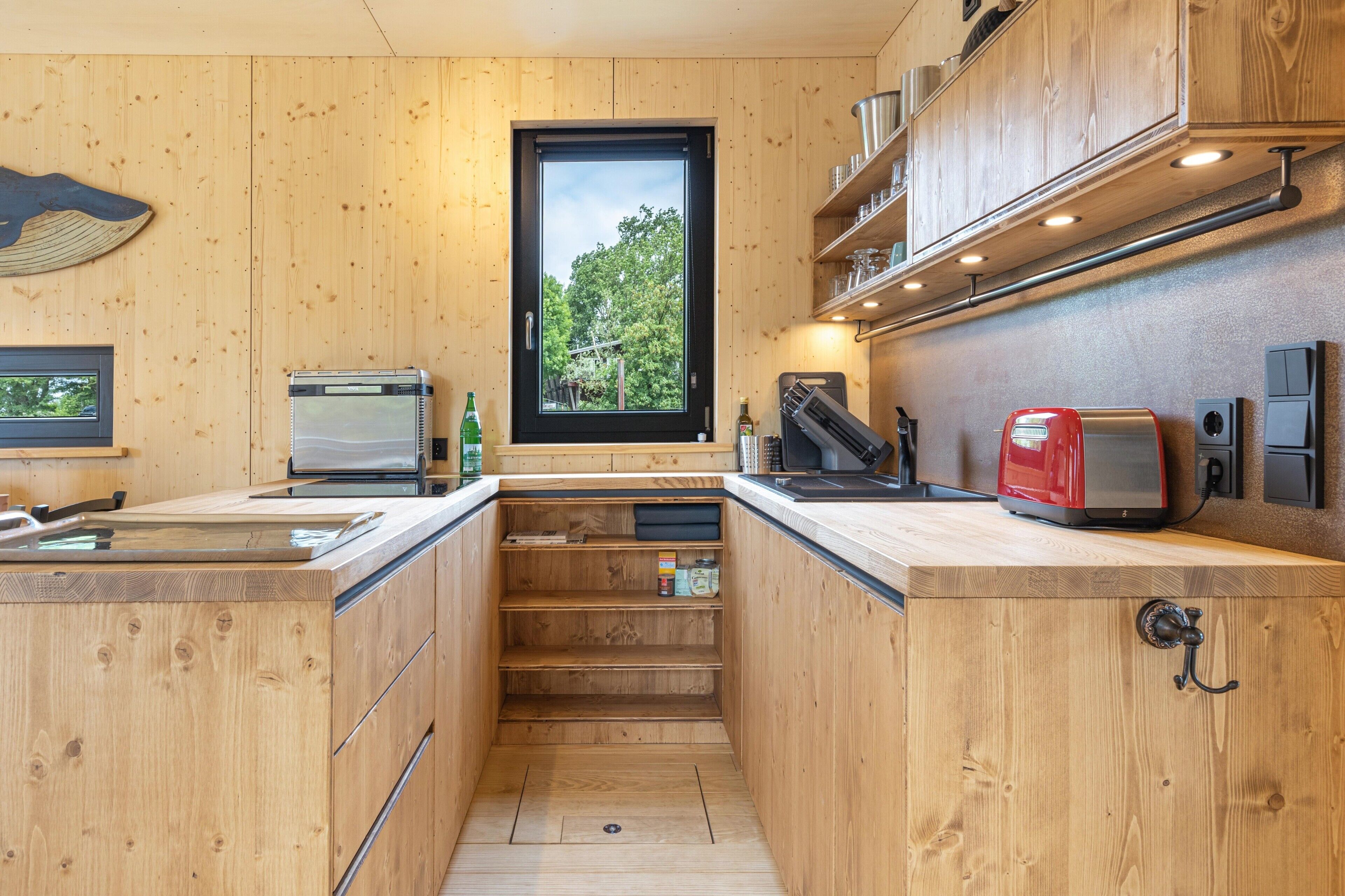 Una cocina compacta con armarios de madera, horno integrado, tostadora y ventana con vistas a árboles.