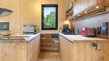 Una cocina compacta con armarios de madera, horno integrado, tostadora y ventana con vistas a árboles.