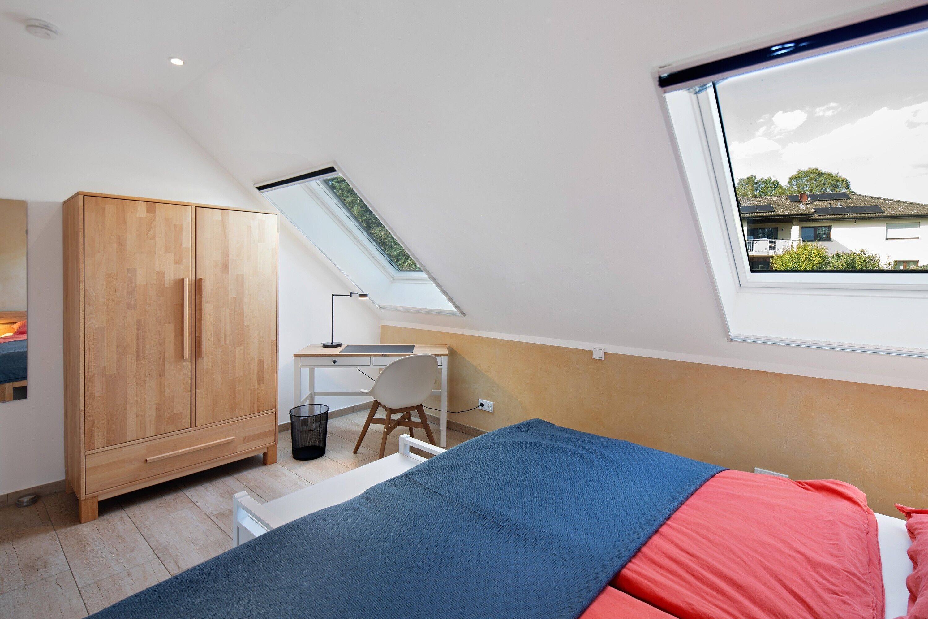A bedroom with a skylight, a bed, a desk, and a wardrobe.