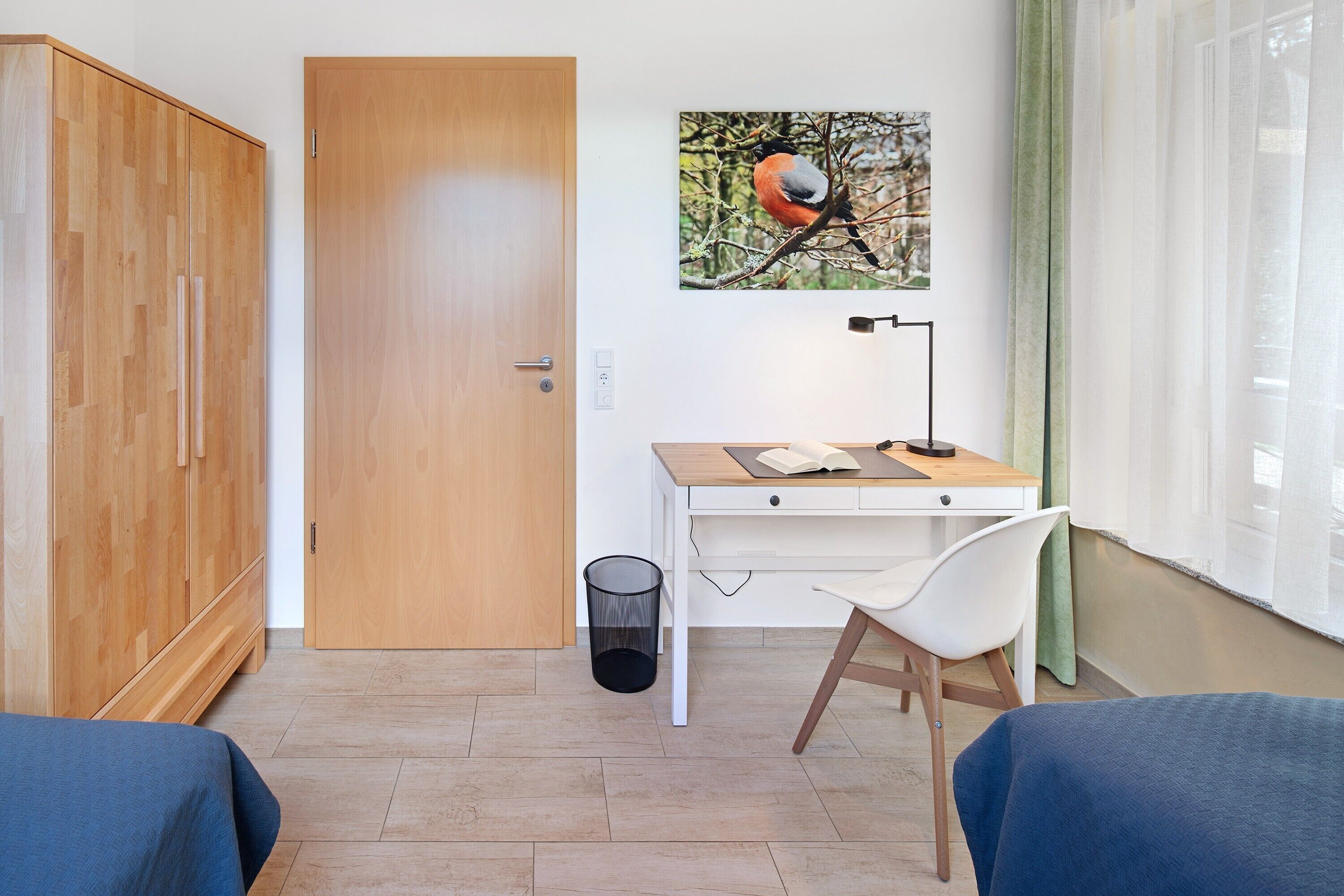 Une chambre avec une armoire en bois, un bureau avec une chaise, un lit et une fenêtre avec des rideaux.