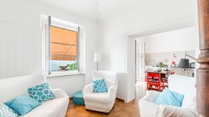 Un salón luminoso con muebles blancos, una ventana con persiana naranja y vistas al exterior.