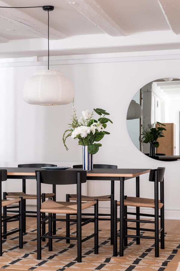 A dining area with a round table and six chairs, a vase with flowers, and a pendant light above.