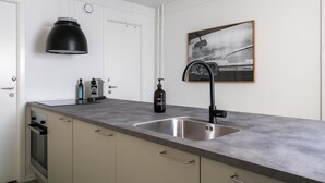 A modern kitchen with a grey countertop, stainless steel sink, and a black pendant light. - Kings Square 2BR Courtyard by Daniel&Jacob's (København)