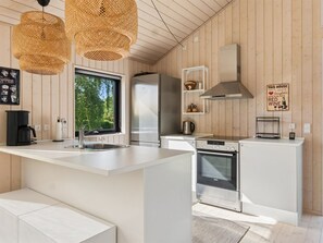 A modern kitchen with a large island, stainless steel appliances, and a view of greenery outside.