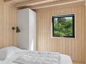 Ein Schlafzimmer mit einem Bett, einem weißen Kleiderschrank, einem Fenster mit Blick ins Grüne und einer Wandlampe.
