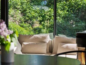 A room with a sofa, a table, and a view of greenery outside.