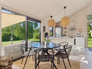 A modern kitchen with a central island, large windows, and a dining area with a round table and chairs.