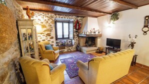 Ein rustikales Wohnzimmer mit Steinwänden, Holzbalken, einem Kamin, einem Fernseher und gelben Sesseln.