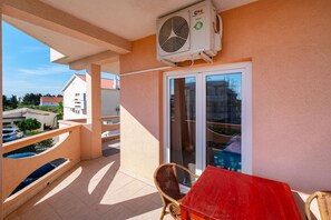 Een balkon met een rode tafel, een rieten stoel en een airconditioning.