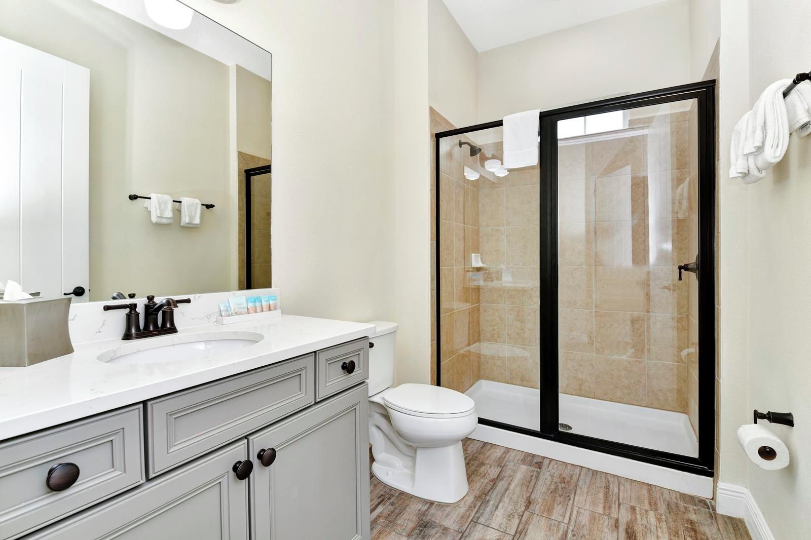 Un baño moderno con lavamanos blanco, grifos de tonos oscuros, inodoro y zona de ducha con mampara de vidrio.