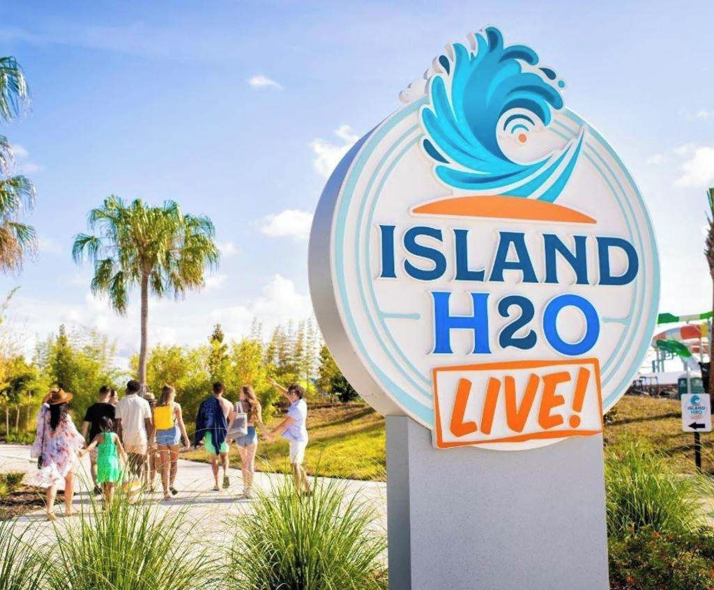 A sign with the text 'ISLAND H2O LIVE!' surrounded by palm trees and people.