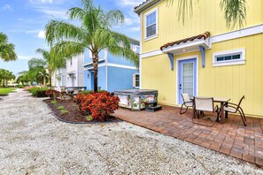 A residential property with a patio area featuring a grill, outdoor seating, and a well-maintained garden with palm trees and red flowers.