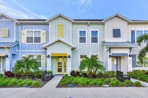 A row of townhouses with a central entrance, each with a small front yard and palm trees.