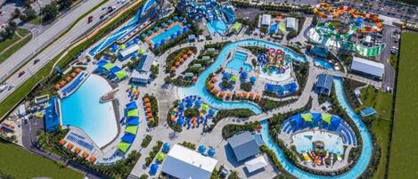 Vista aérea de un parque acuático con varias piscinas, toboganes y un amplio estacionamiento.
