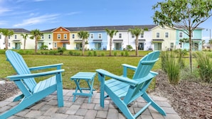 Una hilera de casas de pueblo coloridas con un césped y una zona de estar con sillas Adirondack.