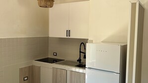 Ett kök med vita skåp, en diskho i rostfritt stål, en inbyggd ugn och en hängande lampa.