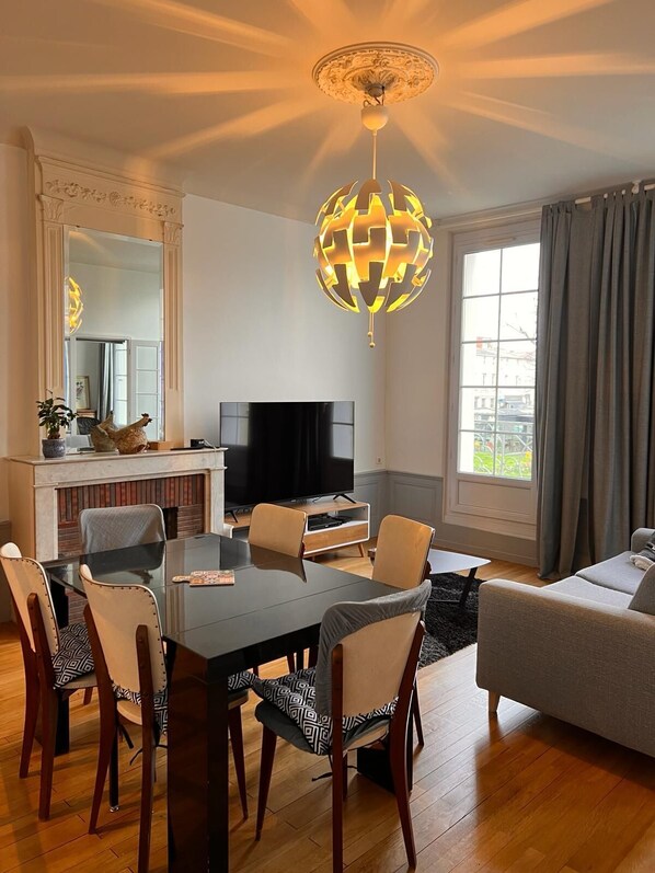 A modern living room with a dining table, chairs, a sofa, a TV, and a decorative globe light. - La Colbertine - Appart Cosy Ultra Équipé @ Place Mythique de Sœurs Jumelles (Rochefort)