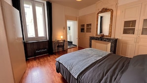 A bedroom with a bed, a desk, a chair, a fireplace, and a large mirror.