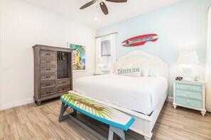 A bedroom with a bed, a bench, a dresser, a nightstand, a ceiling fan, and a surfboard decoration.