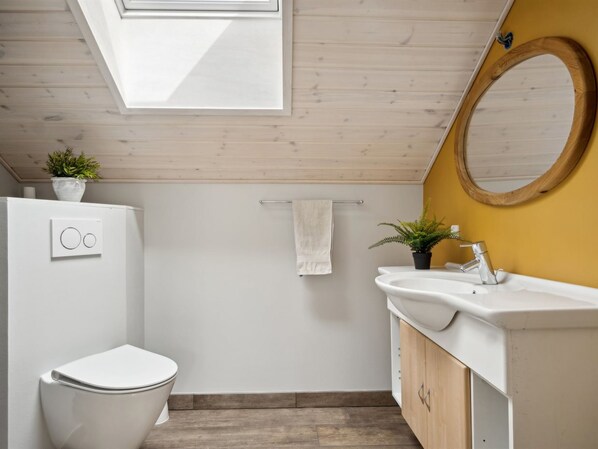 A modern bathroom with a skylight, a toilet, a sink with a mirror, and a towel rack.