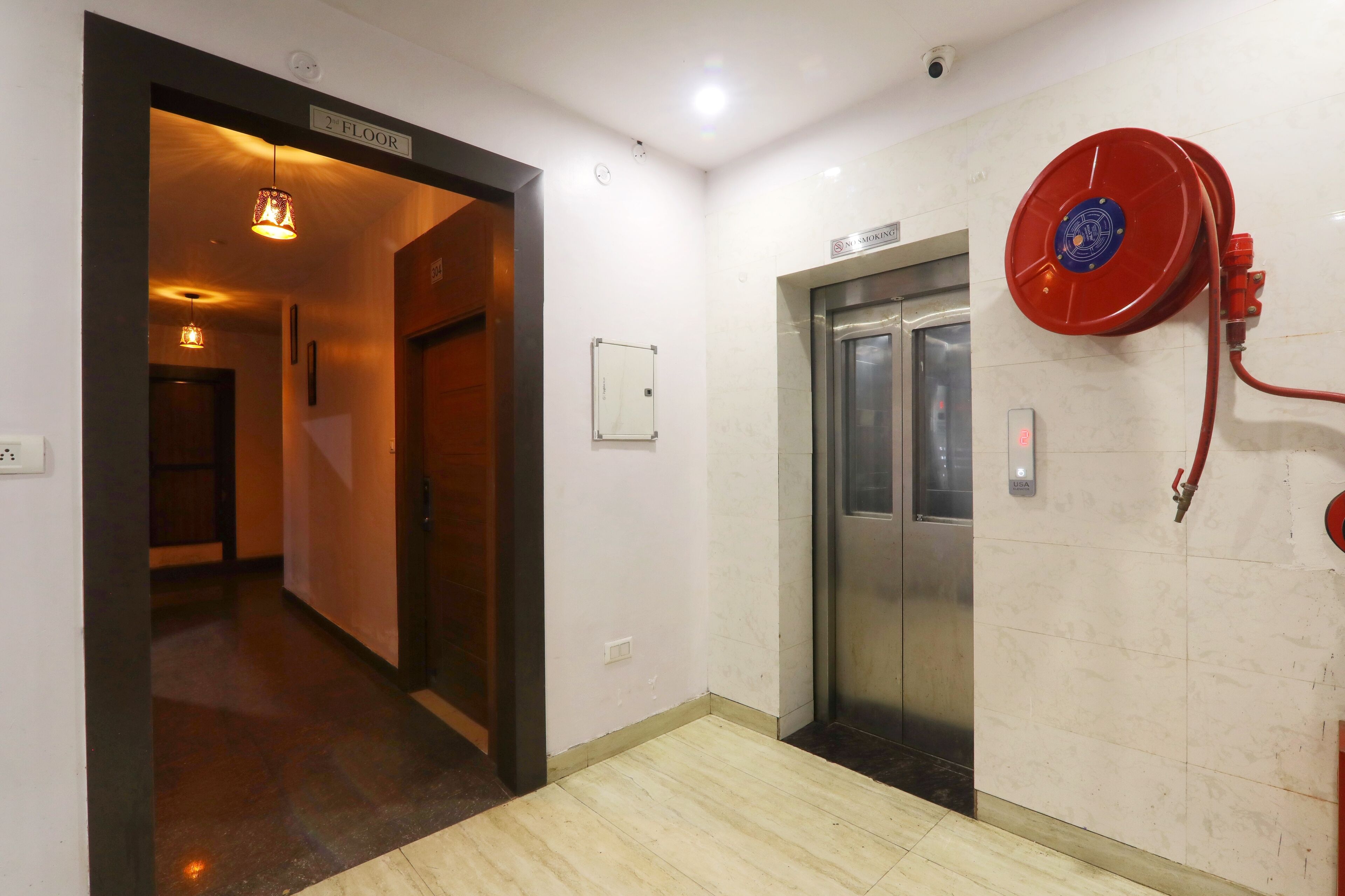 A hallway with a sign indicating the 2nd floor, an elevator, and a fire hose reel on the wall.