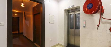 A hallway with a sign indicating the 2nd floor, an elevator, and a fire hose reel on the wall.