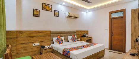 Habitación de hotel con cama de madera, mesita de noche, silla verde, ventilador de techo y aire acondicionado.