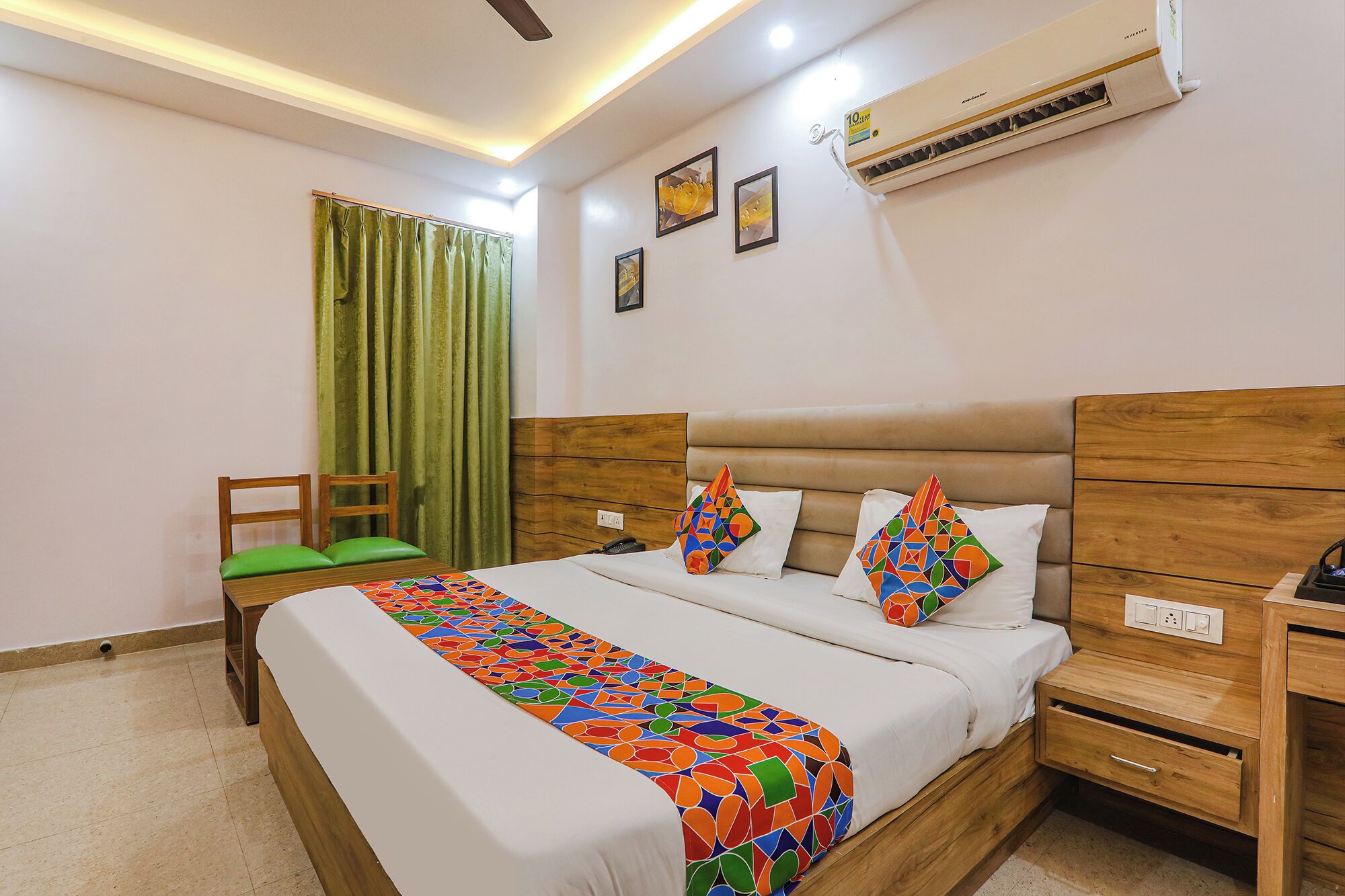 A bedroom with a bed, wooden headboard, bedside tables, a chair, a window with curtains, and an air conditioning unit.